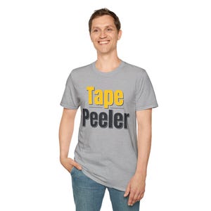 May include: A heather gray short-sleeve t-shirt featuring the text Tape in yellow letters above the word Peeler in black letters. The shirt has a crew neckline and a standard fit, providing a simple and clean look for casual daily wear.