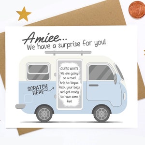 May include: A white and blue camper van with a scratch-off panel that says "Guess what! We are going on a road trip to Vegas! Pack your bags and get ready to have some fun!"  The text "Scratch Here" is on the side of the van with an arrow pointing to the scratch-off panel.