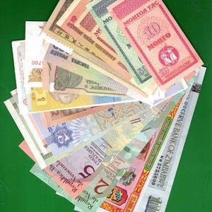 May include: A collection of international paper currency banknotes arranged in a fan shape. The bills feature various colors, intricate patterns, and text in multiple languages, including Mongolian, English, Spanish, and Arabic, representing diverse global denominations.