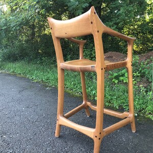 May include: A wooden chair with a unique design, featuring a high back and a curved seat. The chair is made of light brown wood and has a natural finish.
