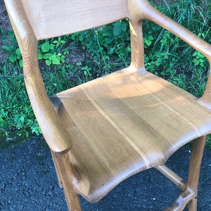 May include: A wooden chair with a curved back and arms. The chair is made of light-colored wood and has a natural finish.