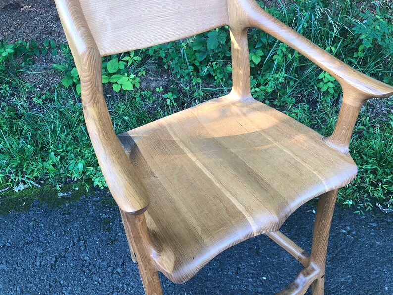 May include: A wooden chair with a curved back and arms. The chair is made of light-colored wood and has a natural finish.