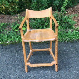 May include: A wooden chair with a simple design, featuring a high back and arms. The chair is made of light brown wood and has a natural finish.