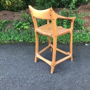 May include: A wooden bar stool with a unique, curved design. The stool is made of light brown wood and has a natural finish. The stool has a simple, yet elegant design.