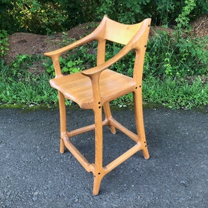 May include: A wooden chair with a unique design, featuring a high back and curved arms. The chair is made of light brown wood and has a natural finish.