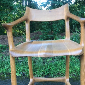 May include: A wooden chair with a unique, organic design. The chair has a high back and arms, and the seat is made of solid wood. The chair is finished in a natural wood stain.