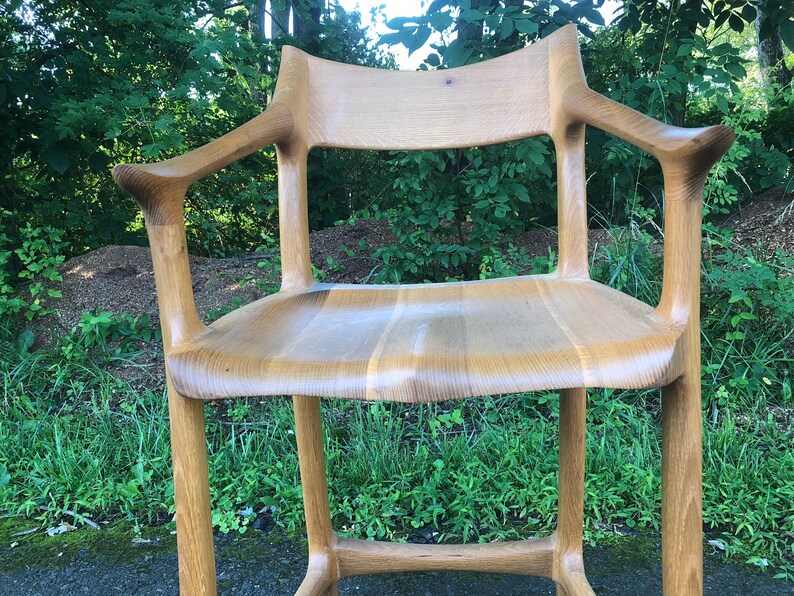 May include: A wooden chair with a unique, organic design. The chair has a high back and arms, and the seat is made of solid wood. The chair is finished in a natural wood stain.