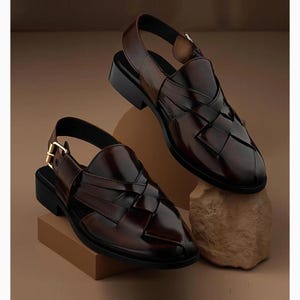 K&ouml;nnte beinhalten: Ein Paar dunkelbraune Ledersandalen mit geflochtenem Obermaterial, geschlossener spitzer Zehenpartie und einem Fersenriemen mit goldfarbener Metallschnalle. Die Sandalen haben einen flachen schwarzen Absatz und eine polierte, gl&auml;nzende Oberfl&auml;che.