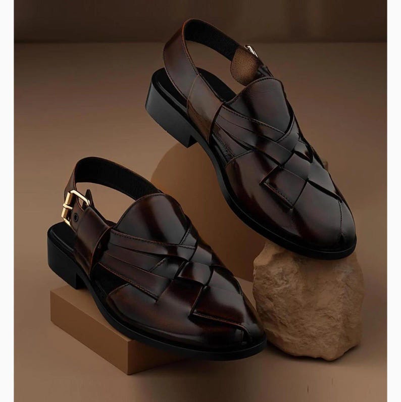K&ouml;nnte beinhalten: Ein Paar dunkelbraune Ledersandalen mit geflochtenem Obermaterial, geschlossener spitzer Zehenpartie und einem Fersenriemen mit goldfarbener Metallschnalle. Die Sandalen haben einen flachen schwarzen Absatz und eine polierte, gl&auml;nzende Oberfl&auml;che.