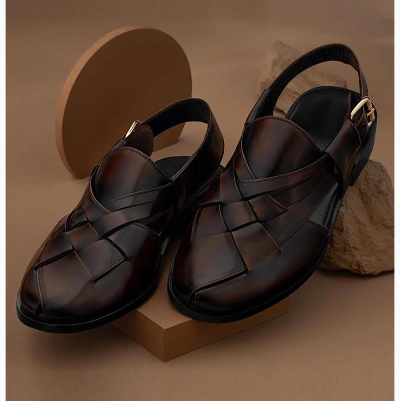 K&ouml;nnte beinhalten: Ein Paar dunkelbraune Ledersandalen mit geflochtenem Riemendesign auf der Oberseite, geschlossener Zehenpartie und einem verstellbaren Fersenriemen mit goldfarbener Metallschnalle. Das Leder hat eine polierte, gl&auml;nzende Oberfl&auml;che mit Schattierungen.