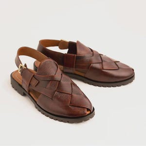 May include: A pair of dark brown leather sandals featuring a woven upper design, a closed-toe construction, and an adjustable ankle strap with a gold-toned metal buckle. The footwear includes a thick, dark brown lugged sole for added traction.