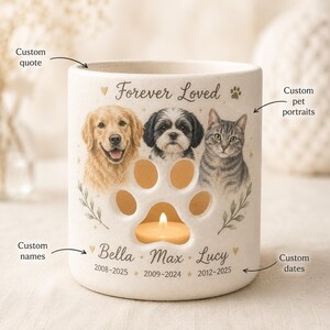 Könnte beinhalten: Ein zylindrischer, cremefarbener Kerzenhalter aus Keramik mit einer pfotenförmigen Aussparung. Die Vorderseite zeigt den Text Forever Loved, Porträts eines Golden Retrievers, eines Shih Tzus und einer getigerten Katze sowie Namen und Daten.