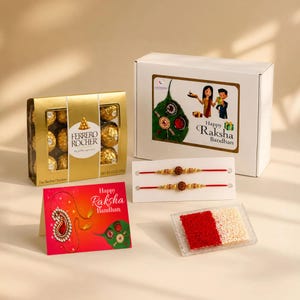 May include: A gift set for Raksha Bandhan including a box of Ferrero Rocher chocolates, two red thread bracelets with gold and brown beads, a greeting card with the text Happy Raksha Bandhan, and a small container of red and white powder.