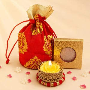 May include: A red drawstring pouch with gold floral patterns, a square gold textured box containing a circular silver coin, and a yellow flower-shaped tea light candle in a gold lattice holder on a red and gold circular base with flower petals.