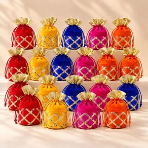 May include: A collection of small drawstring pouches in red, yellow, blue, pink, and orange velvet. Each pouch features a gold metallic lattice pattern on the lower half and a gold metallic ruffled top edge with matching drawstring cords.