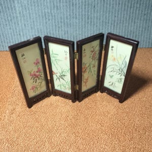 Op de afbeelding: Een vierdelig vouwscherm met donkerbruine houten frames en lichtgekleurde panelen. Elk paneel toont een unieke botanische illustratie met verfijnde bloem- en bamboemotieven, geaccentueerd door zwarte kalligrafische teksten en rode stempels.