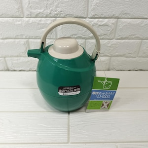 May include: A round, dark green thermal carafe with a beige lid and handle. The carafe features a black label with Japanese text and a green tag with an elephant logo, the text "象印ポットきゅうす VJ-1000", and an "X" symbol. The body is smooth and spherical.