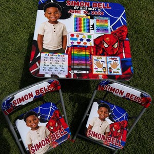 May include: A square table and two folding chairs featuring a Spider-Man theme, personalized with the name Simon Bell and birth date June 10, 2022. The set includes educational graphics like the alphabet, numbers, colors, and days of the week.