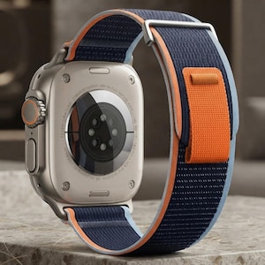 May include: A silver-toned smartwatch with a circular sensor array on the back casing. The watch features a fabric strap in navy blue with bright orange accents and a light blue trim, secured by a silver metal buckle and an orange fabric loop.