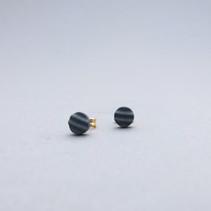 Puede incluir: Un par de pequeños pendientes redondos grises con una superficie texturizada.