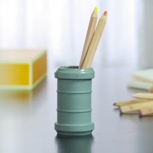 May include: A grey pencil holder made from a pipe fitting with two wooden pencils inside. One pencil has a yellow eraser and the other has an orange eraser.