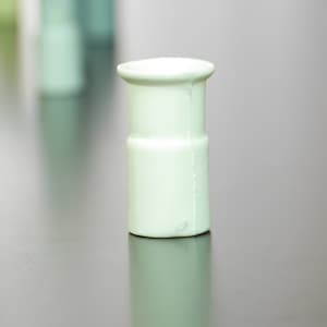 Puede incluir: Un jarrón de cerámica blanco con un diseño sencillo. El jarrón es alto y delgado, con una base redondeada y una parte superior ligeramente acampanada.