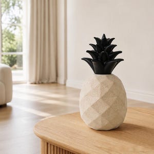 May include: A decorative pineapple-shaped object featuring a beige, speckled, faceted base and a smooth, solid black top section representing the leaves. The item has a geometric, multi-sided structure and stands upright as a singular piece.