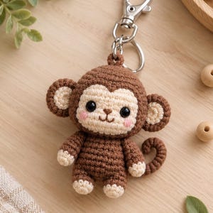 Peut inclure: Un porte-clés singe en crochet marron et crème avec une tête ronde, des yeux de sécurité noirs, des joues brodées en rose, un petit nez marron et une queue enroulée. Le singe est fixé à un mousqueton et un anneau en métal argenté.