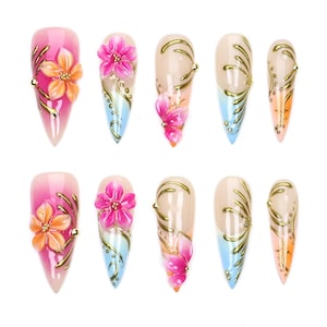 Può includere: Un set di dieci unghie finte a stiletto con una base sfumata rosa, blu e color carne. I disegni includono accenti floreali 3D in rilievo rosa e arancioni, intricati dettagli a linee metalliche dorate e piccole decorazioni a perline dorate.