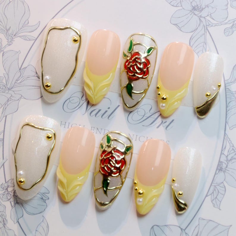 May include: A set of ten artificial nails with various designs. Some nails are white with gold accents, others are peach with yellow tips, and two feature a red rose design. The words "Nail Art" are visible.