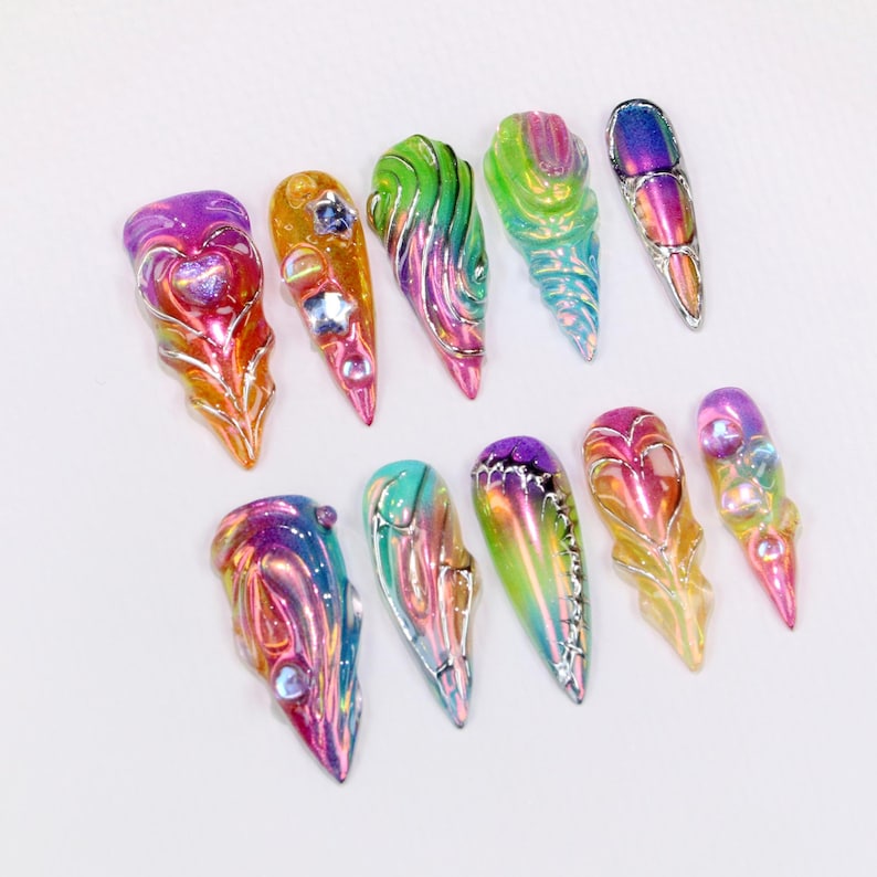 May include: A collection of iridescent, sculpted nail art designs. Each nail features a unique shape and color gradient, with accents of silver and embedded rhinestones. The designs include heart, swirl, and abstract patterns, showcasing a variety of vibrant colors.