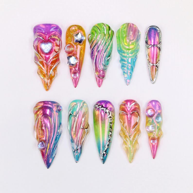 May include: A collection of ten iridescent, sculpted nail art designs. Each nail features a unique design with a variety of colors, including pink, purple, green, and silver. Some nails have heart, star, and gem embellishments.