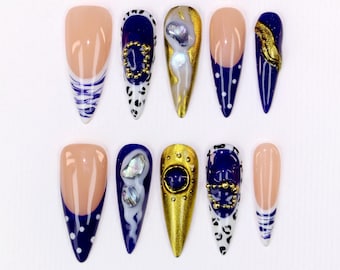 May include: A set of ten artificial nails with various designs. Some nails feature a nude base with white and blue stripes or dots. Others have a navy blue base with gold accents, pearls, and leopard print details. The nails are almond-shaped.