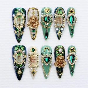Peut inclure: Dix charmes d'art pour ongles de couleur verte et dorée, présentant une variété de motifs, notamment des cœurs, des anges et des images religieuses. Les charmes sont conçus pour être appliqués sur les ongles.