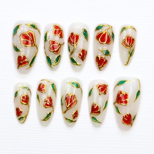 May include: Set of ten false nails with a white base and a floral design featuring red and gold flowers and green leaves.