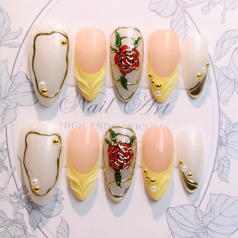 May include: A set of ten artificial nails with a variety of designs. Some nails are pearlescent white with gold trim and small gold accents. Others feature a yellow base with a peach-colored tip, and some have a red rose design.