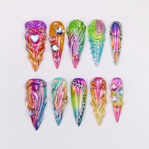 May include: A collection of ten iridescent, sculpted nail art designs. Each nail features a unique shape and color palette, including pink, orange, green, and blue. Some nails have embedded embellishments like stars and hearts.