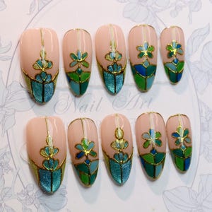 May include: Set of ten artificial nails with a light pink base, featuring gold outlines and intricate designs in teal, green, and blue. The nails have a glossy finish and a variety of floral and geometric patterns.