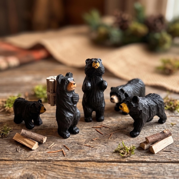May include: A set of five black bear figurines carved from wood, featuring textured surfaces and tan-colored snouts. One bear stands upright carrying a bundle of small logs on its back, while the others are depicted in various standing and walking poses.