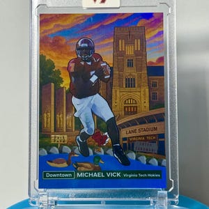 May include: A Michael Vick Virginia Tech Hokies Downtown sports trading card encased in a clear plastic holder with a VT logo sticker. The card features an illustration of a football player, Lane Stadium, and a duck pond under a sunset sky.