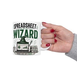 May include: A white ceramic mug featuring the text SPREADSHEET WIZARD in green and black. The graphic includes a laptop with a spreadsheet, a wizard hat, a wand, and books labeled VLOOKUP, PIVOT TABLES, IF() LOGIC, and SUMMON DATA.