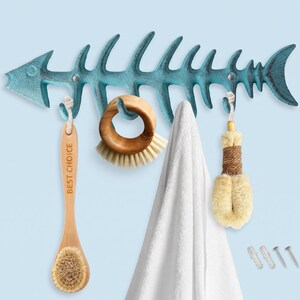 May include: A teal fish skeleton wall hook rack with a distressed finish. Hanging from the hooks are a wooden brush with the text BEST CHOICE, a round wooden scrub brush, a white towel, and a natural fiber brush. Two wall anchors and screws.