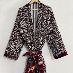 May include: A long-sleeved robe featuring a black and beige leopard print pattern. The garment includes a deep burgundy belt and matching cuffs adorned with a tropical animal and leaf motif. The interior lining displays a black and white vertical stripe.