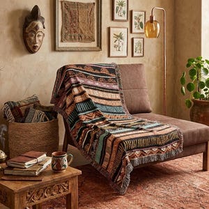 May include: A woven throw blanket featuring a multi-colored pattern of horizontal stripes, geometric shapes, and scalloped motifs in shades of black, orange, teal, and cream, draped over a brown upholstered chaise lounge chair.