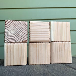 May include: Six light-colored wooden blocks arranged in a two-by-three grid. Each block features a distinct natural wood grain pattern, ranging from tight vertical lines to curved, swirling rings, showcasing the raw texture of the light pine wood.