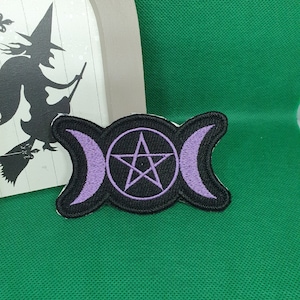 Peut inclure: Un patch brodé noir et violet avec un symbole de triple lune et un pentagramme à l'intérieur. Le patch est sur un fond vert.