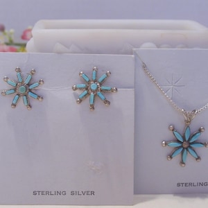 May include: A set of sterling silver earrings and a necklace with turquoise flower pendants. The earrings and pendant are both in the shape of a starburst with turquoise stones.