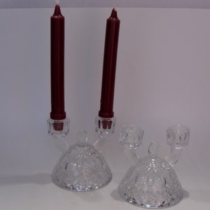 May include: A pair of clear glass candle holders with a diamond pattern. Each holder has two arms and a domed base. The holders are holding two burgundy candles.