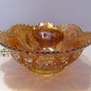 May include: An iridescent orange glass bowl with a scalloped rim. The bowl has a detailed pattern of flowers and geometric shapes. The bowl is approximately 9 inches in diameter and 4 inches tall.