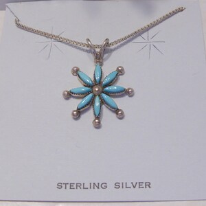 May include: A silver necklace with a turquoise flower pendant. The pendant is made of sterling silver and has a blue turquoise stone in the center. The necklace is on a white background with the words "STERLING SILVER" printed below the pendant.